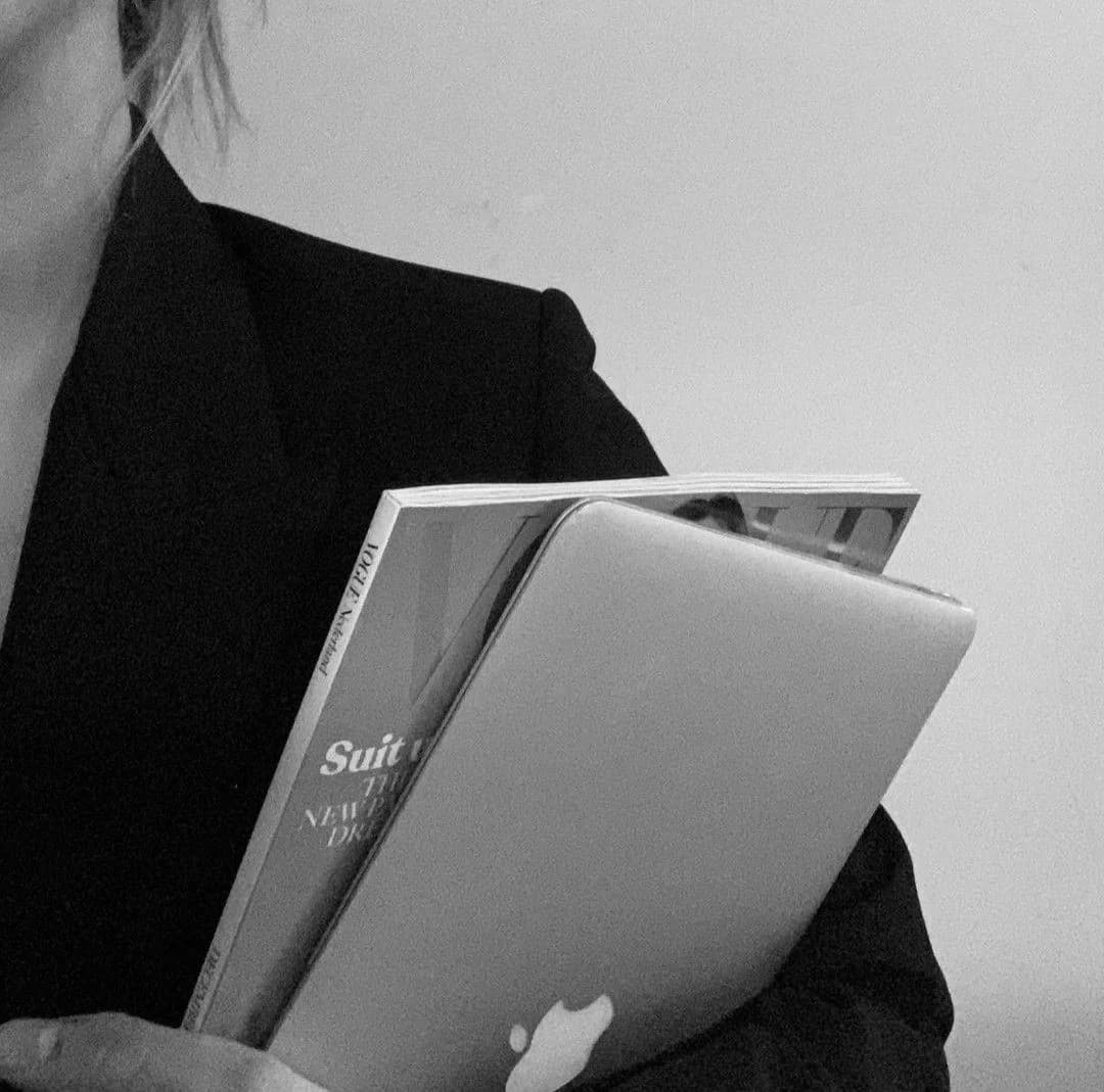 Mulher de blazer preto segurando laptop e revista Vogue em foto preto e branco.